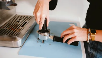 Händedrücken einen Tamper auf Kaffeepulver auf einer Arbeitsfläche.