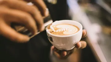 A hand pours milk into a coffee mug in a café.