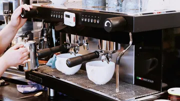 Coffee maker draws espresso in a modern café environment.