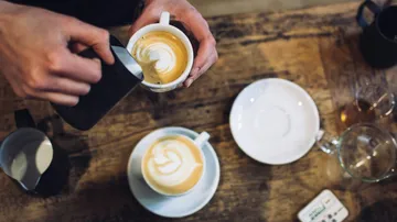 Hands pour microfoam into cups on a table.