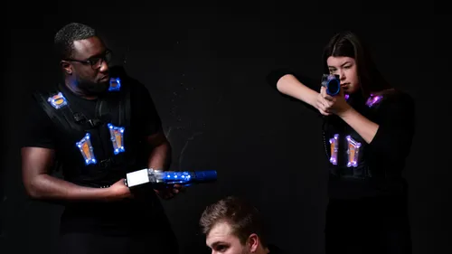 Zwei Personen spielen Lasertag in einem dunklen Raum.