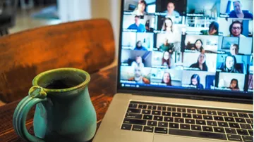 Tasse neben dem Laptop, auf dem die Teilnehmer des Videoanrufs zu sehen sind.