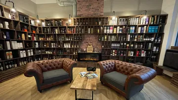 Two Chesterfield sofas stand in front of a bookshelf with bottles.