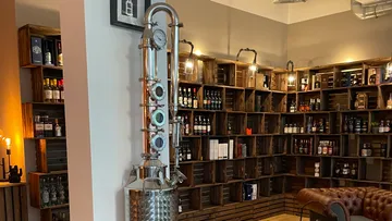 Stainless steel distiller stands in a bottle storage environment.