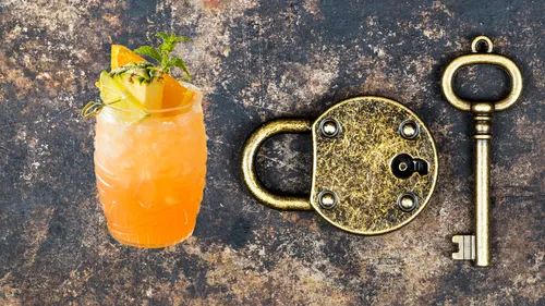 The cocktail glass and key lie next to a lock on metal.