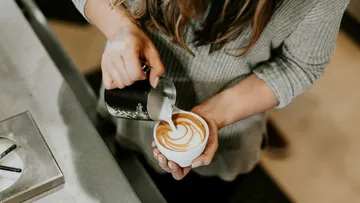 A person pours milk into a cup of coffee.