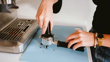 Hands operate a portafilter on a kitchen surface.