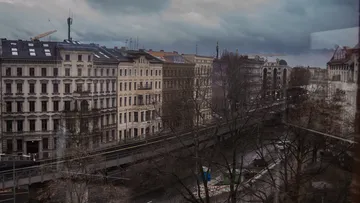 Straße mit Gebäuden, Bäume, Wolken und Baukräne.
