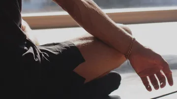 Male arm sits relaxed in sunlight, legs crossed.