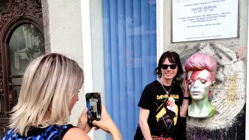 Die Person posiert mit einem Bowie-Wandbild, während sie fotografiert wird.