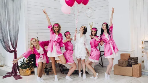 Six women in pink bathrobes celebrate with balloons.