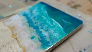 Colorful resin art resembling ocean waves on wood.