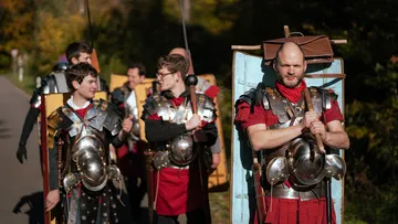 Gruppe von Menschen in römischen Soldatenkostümen, die draußen marschieren.