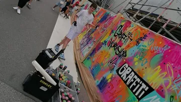 Young man sprays graffiti on a colorful wall.