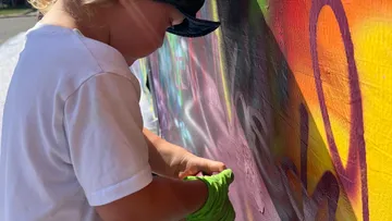 Kind malt mit Spraydose an einer bunten Wand.