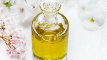 Glasflasche mit Öl, umgeben von Blumen.