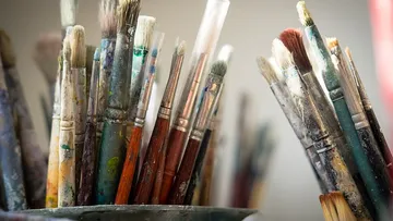 Paintbrushes in containers, covered in paint.