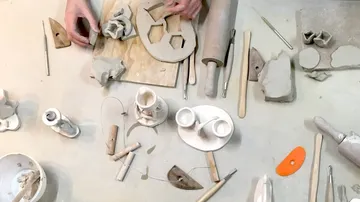Hands sculpt with clay on a workspace table.