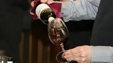 Person pouring red wine into glass.