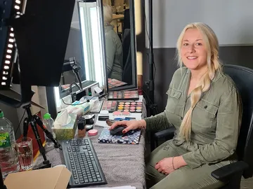 Frau sitzt am Schminktisch mit Make-up und Computertastatur.