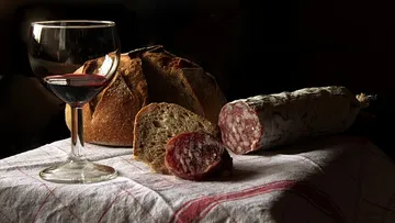 Rotwein, Brot und Salami auf einer Tischdecke.