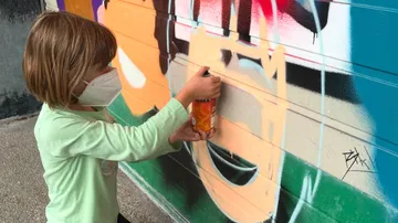 Ein Kind sprüht ein Wandgemälde an die Wand.