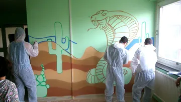 Menschen, die ein Wüsten-Wandbild an die Wand malen.