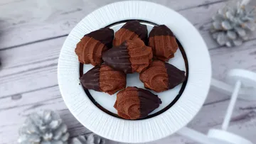 In Schokolade getauchte Orangen-Madeleines auf weißem Teller.