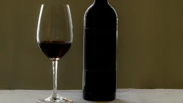 Ein Glas Rotwein und eine Flasche auf dem Tisch.