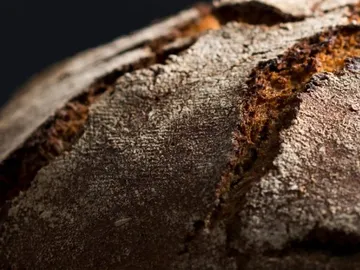 Ein Brot liegt, es hat eine raue, rissige Kruste.