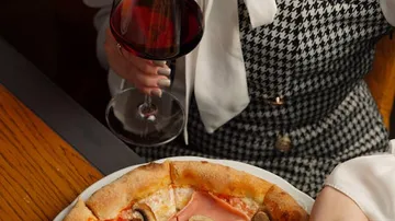Person holding wine near pizza on table.