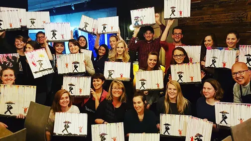 Group holding paintings with umbrella figures indoors.