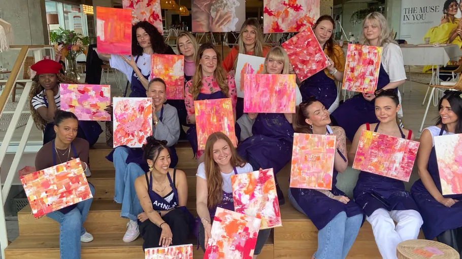 Group holding abstract paintings in vibrant space.