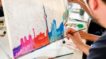Person painting colorful skyline on canvas.