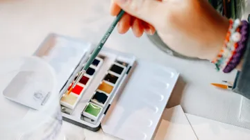 Hand mit Pinsel über der Aquarellpalette.