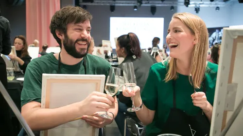 Two people laughing, holding wine glasses, indoor event.