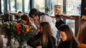 Frauen arrangieren drinnen Blumen an einem Tisch.