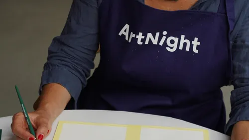 Person wearing 'ArtNight' apron painting paper.