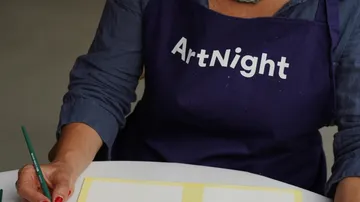 Person wearing 'ArtNight' apron, holding paintbrush.