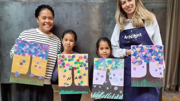 Two adults and two children holding colorful tree paintings.