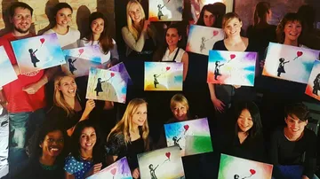 Group of people holding paintings of girl with balloon.