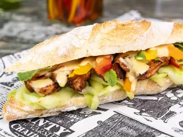 Sandwich mit Gemüse und Fleisch, auf Zeitungspapier serviert.