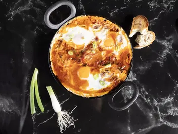 Casserole with eggs on black table with bread next to it.