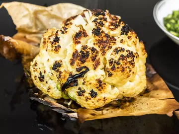 Roasted cauliflower on baking paper, next to a bowl of vegetables.