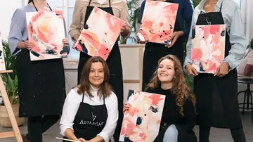 Group of people holding abstract paintings in art class.
