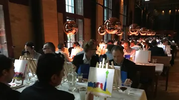 People painting at an event in a dimly lit room.