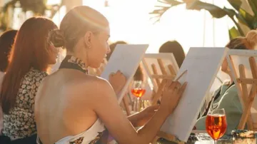 Women painting on canvases in sunlight.