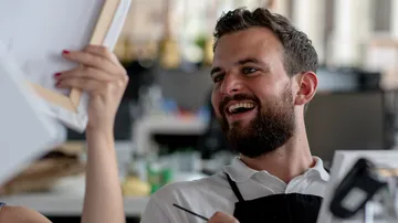 Smiling man holding canvas in a classroom.