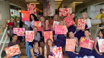 Group of people holding abstract paintings in workshop.