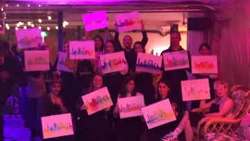 Group holding colorful skyline paintings indoors.